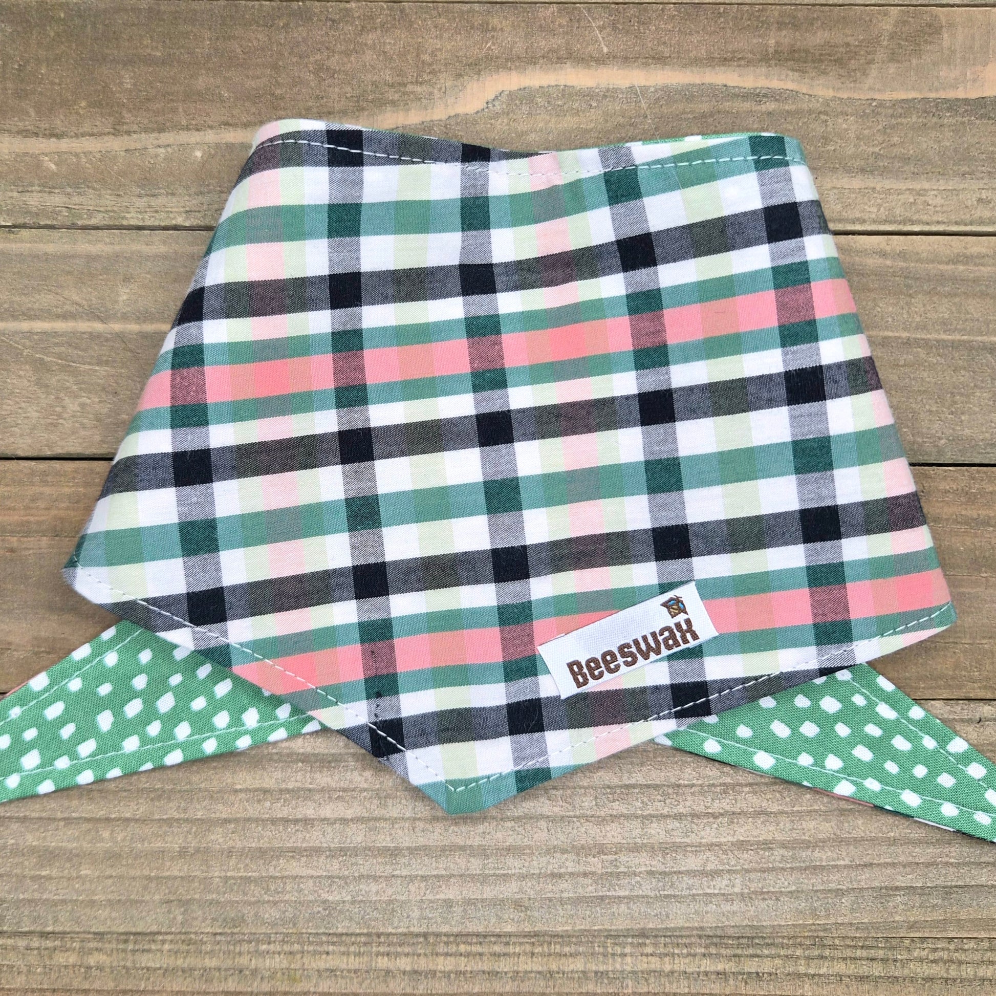 A plaid bandana with a green and white polka dot pattern, featuring a label with the text "Beeswah" on it.