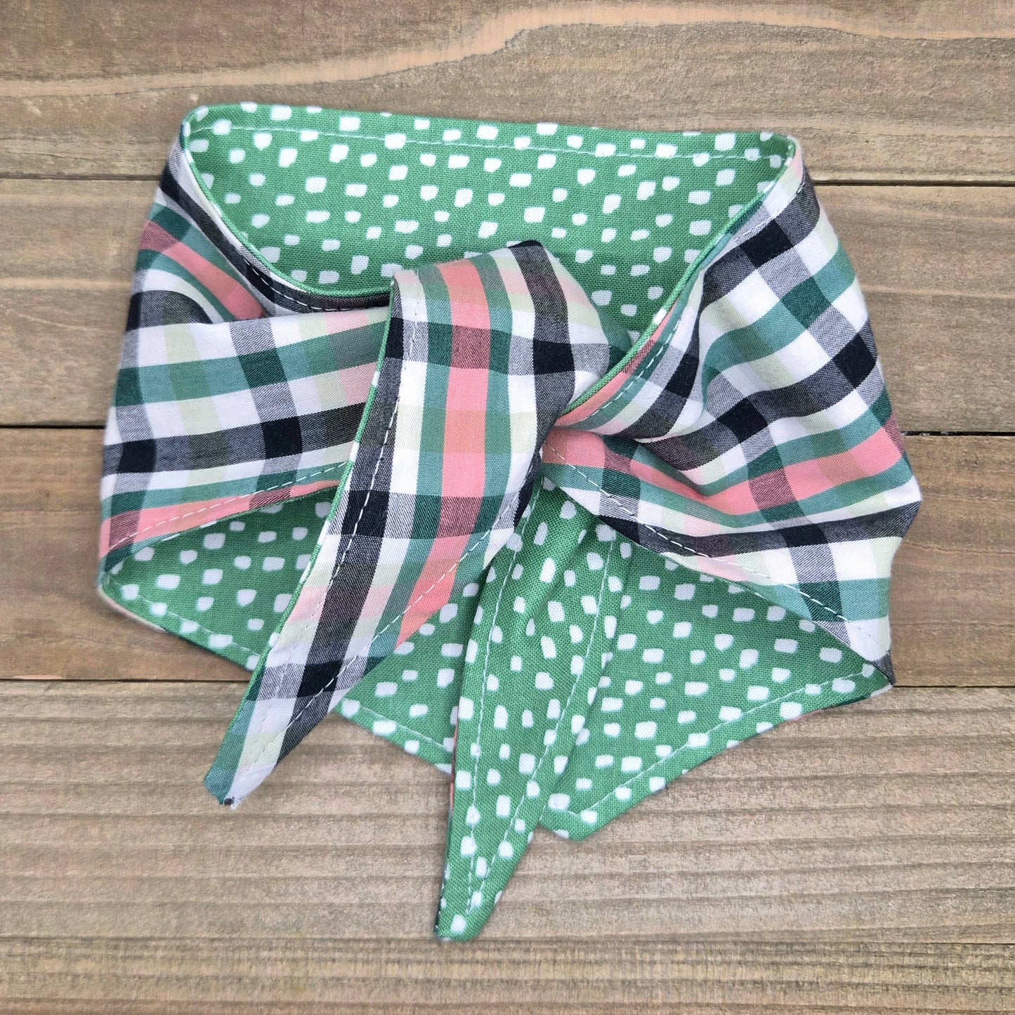 A colorful bandana with a plaid pattern and green polka dots is displayed on a wooden surface.