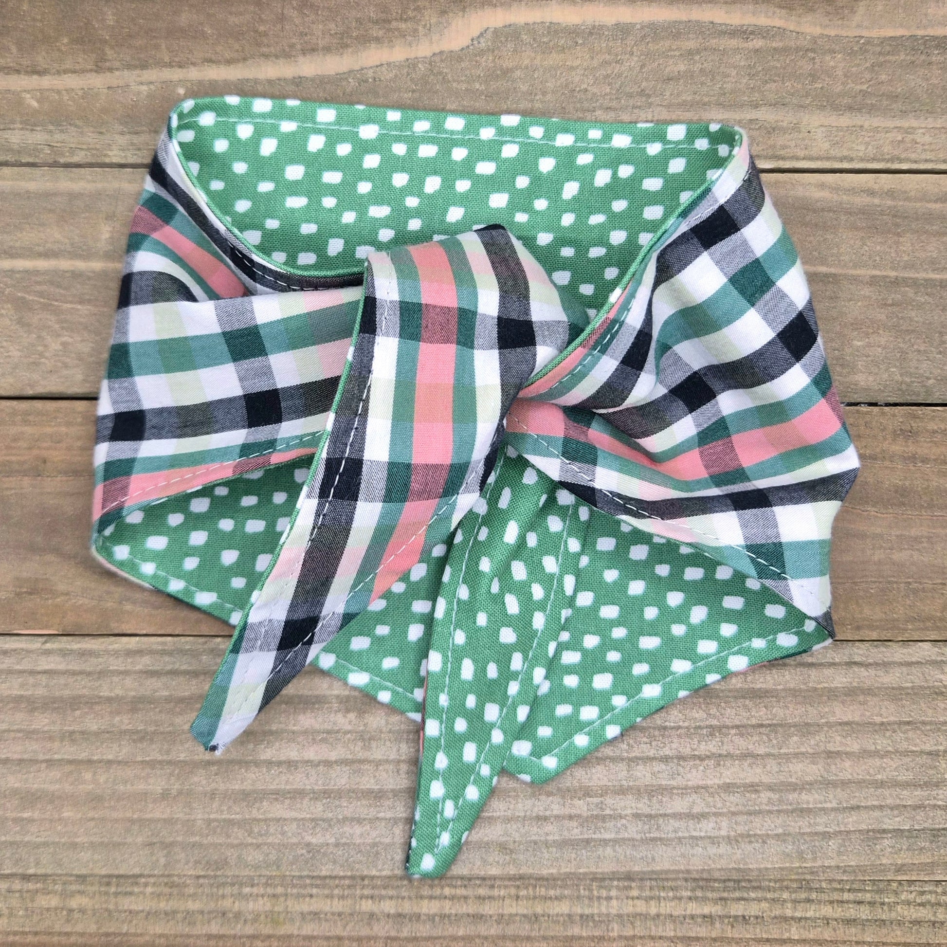 A colorful bandana with a plaid pattern and green polka dots is displayed on a wooden surface.