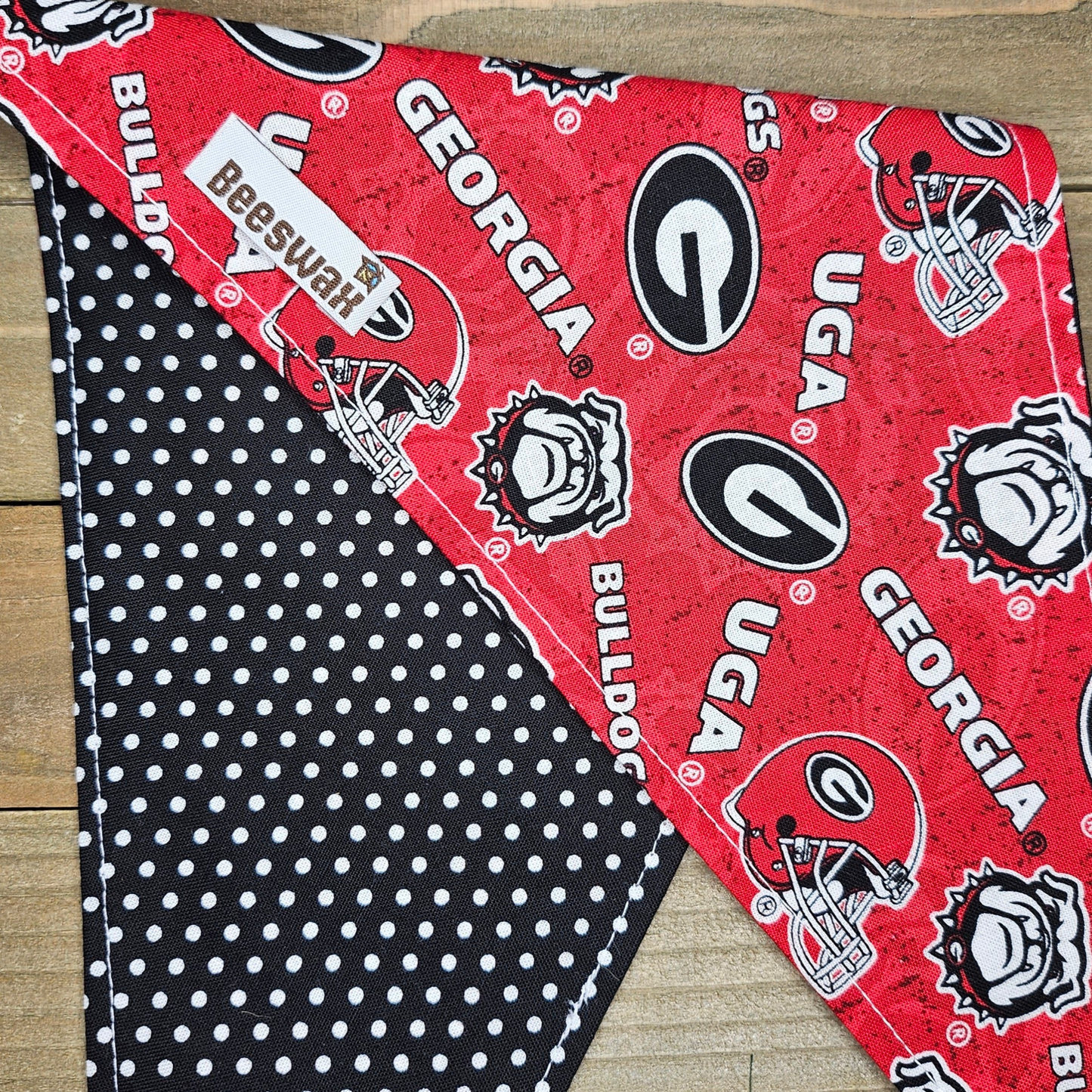 a red and black dog bandana with the Georgia Bulldogs football team logo printed on it, placed on a wooden surface.