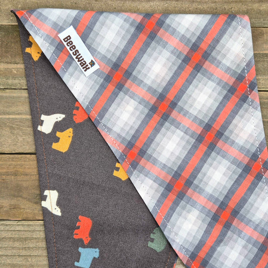 A plaid dog bandana with a gray background and a pattern of bears in various colors, including white, orange, and black.