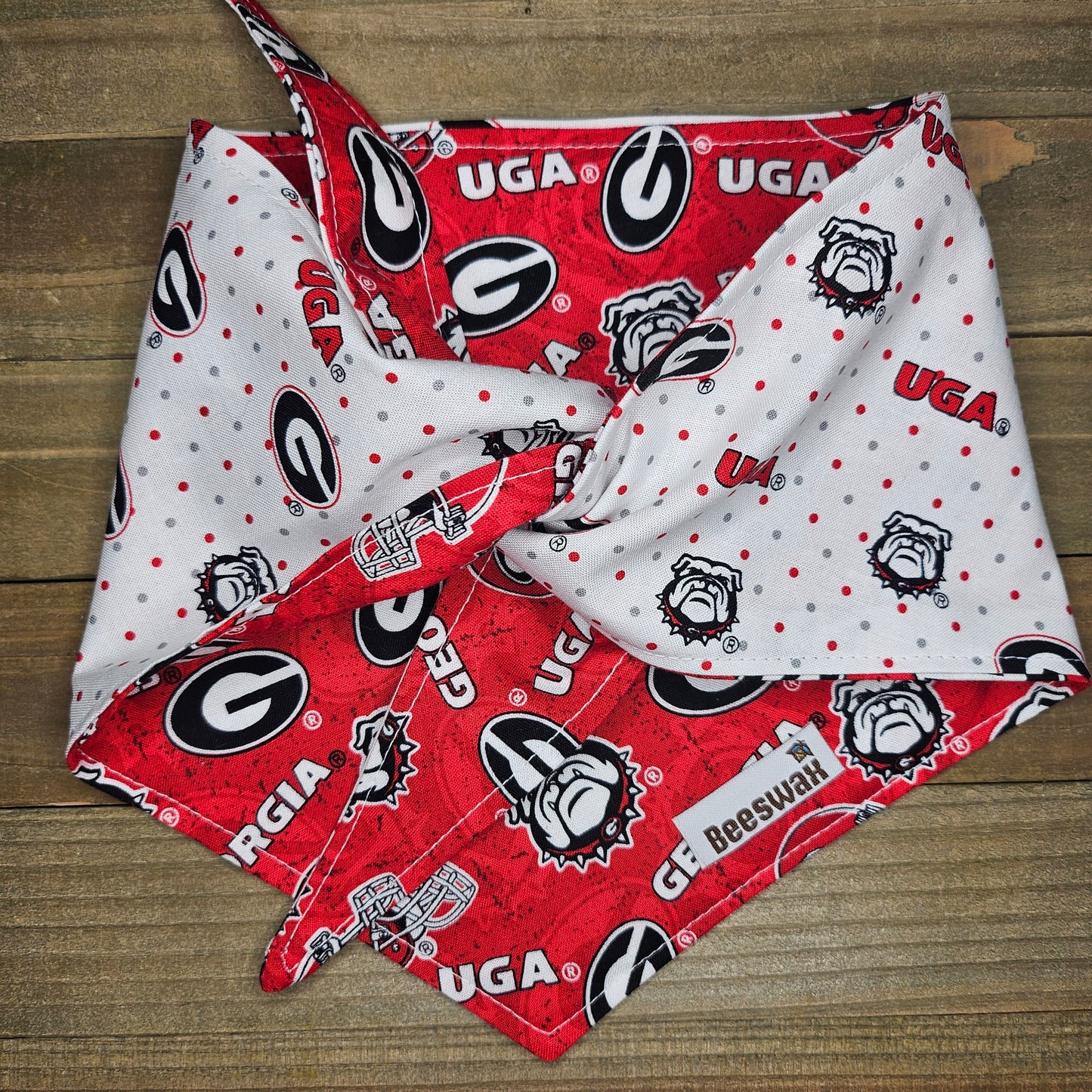 A red and white dog bandana with the Georgia Bulldogs logo printed on it, folded in half and tied around a wooden surface.
