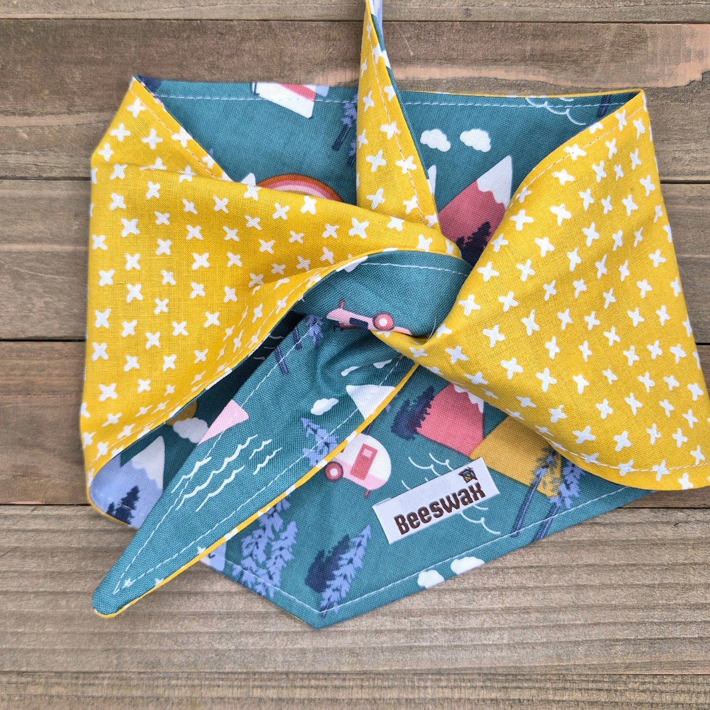 A colorful bandana with a pattern of yellow stars and blue mountains, folded in half and displayed on a wooden surface.
