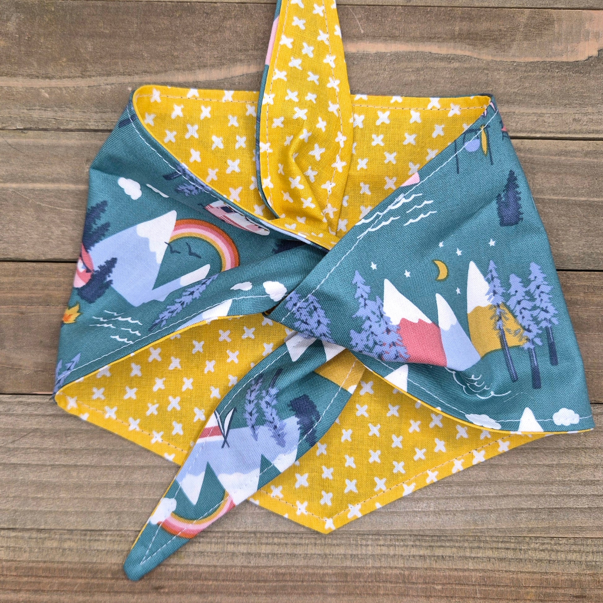 a colorful bandana with a pattern of mountains, trees, and stars on a wooden surface.