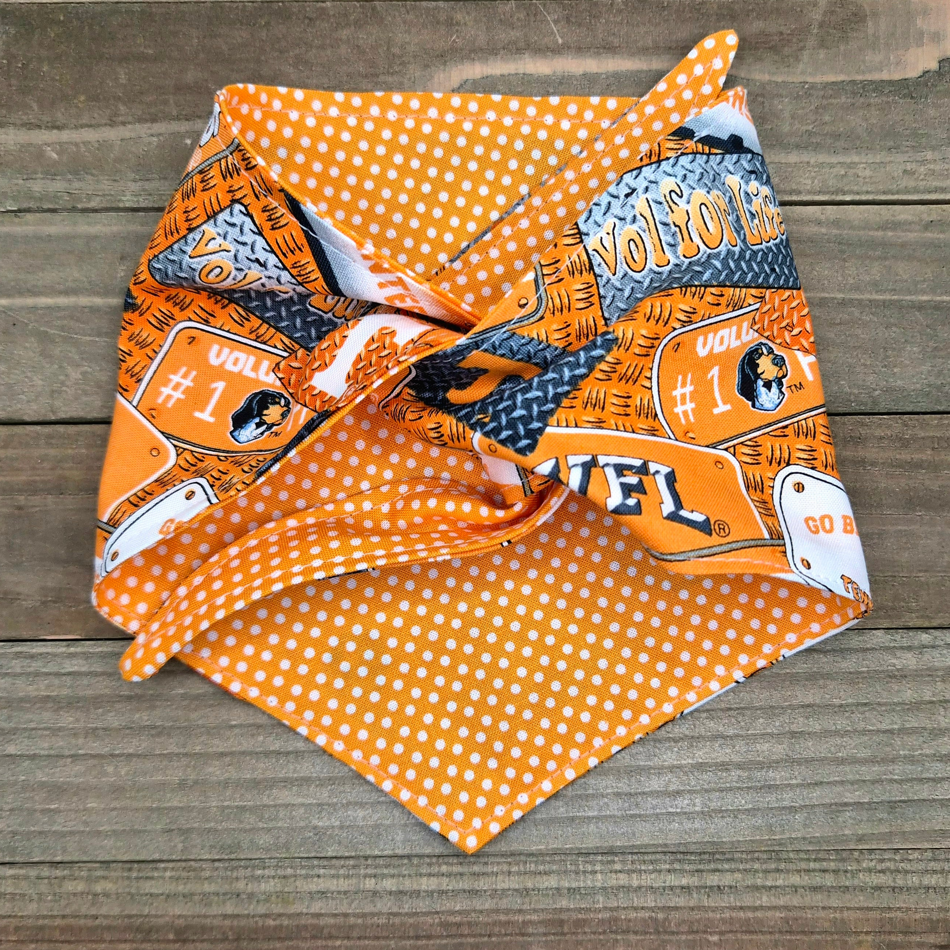 a vibrant orange and white polka dot bandana with various football-related graphics and text, including the word "VOL" and the number "1".