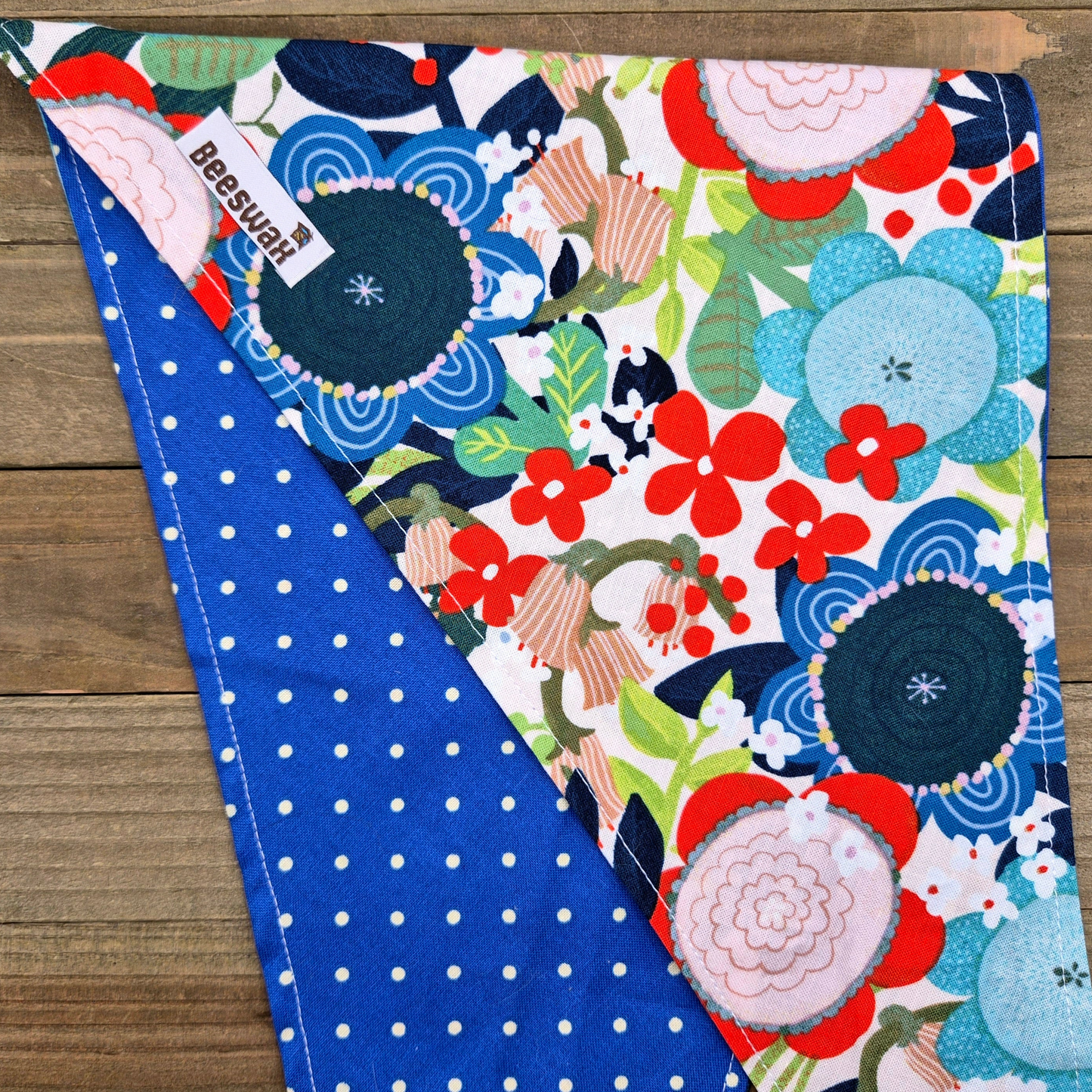 a colorful floral print with red, blue, and white flowers, along with green leaves and stems, laid out on a wooden surface.