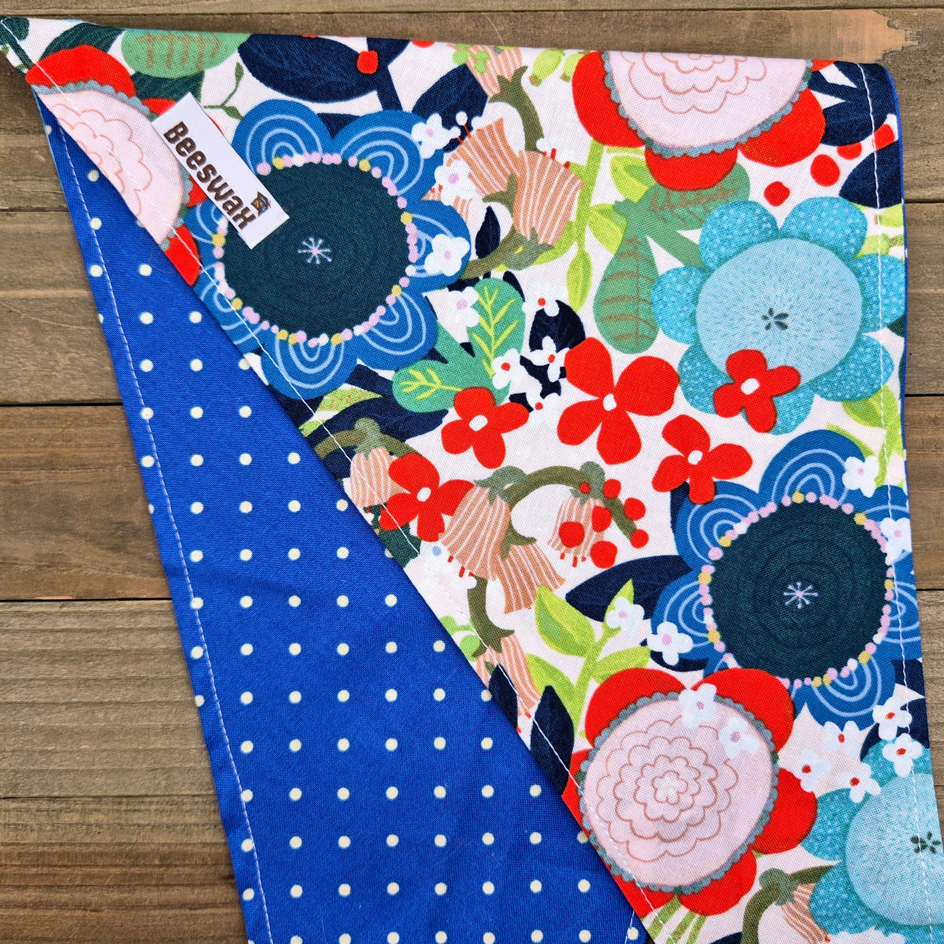a colorful floral print with red, blue, and white flowers, along with green leaves and stems, laid out on a wooden surface.