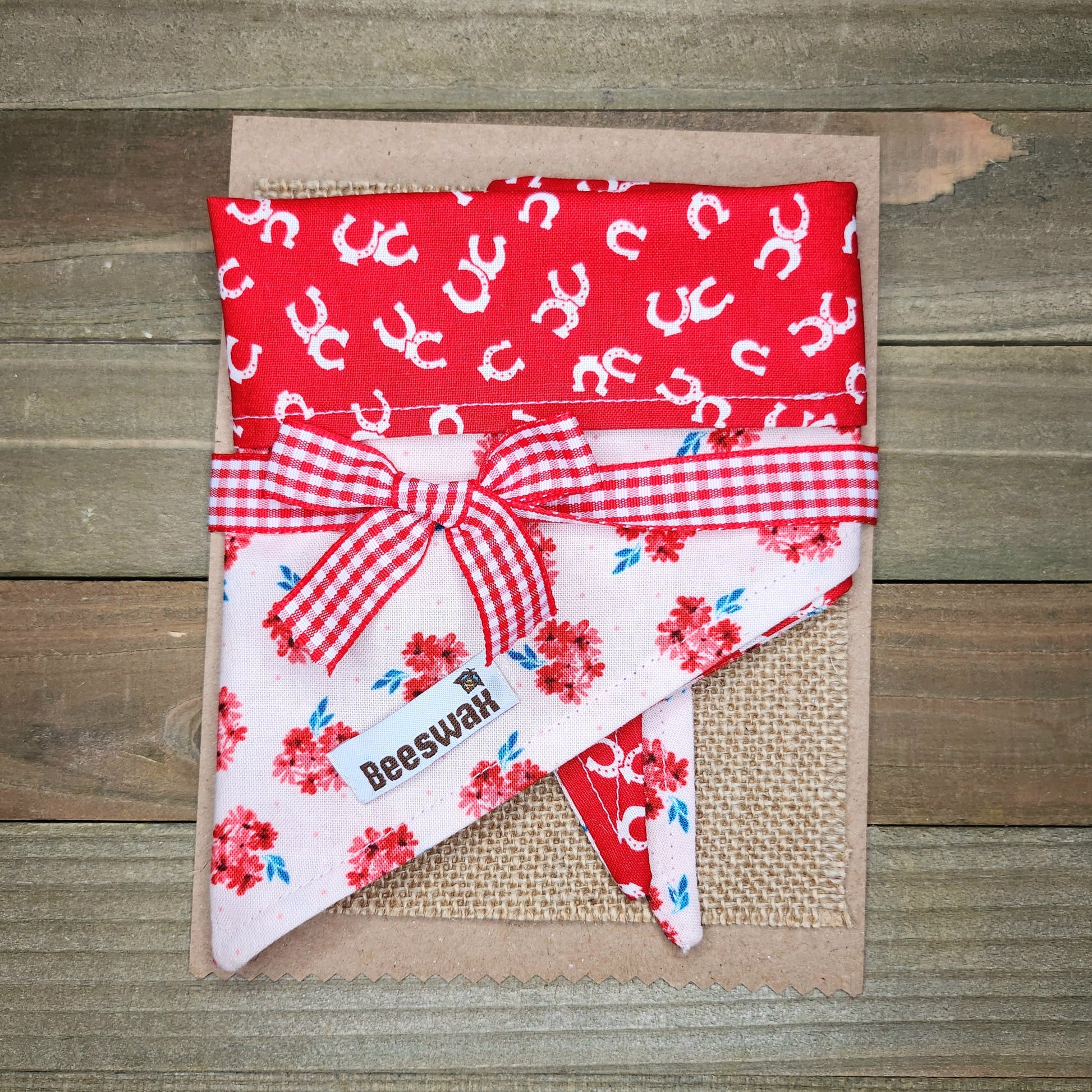 a red and white floral patterned fabric with a red ribbon tied around it, placed on a wooden surface.