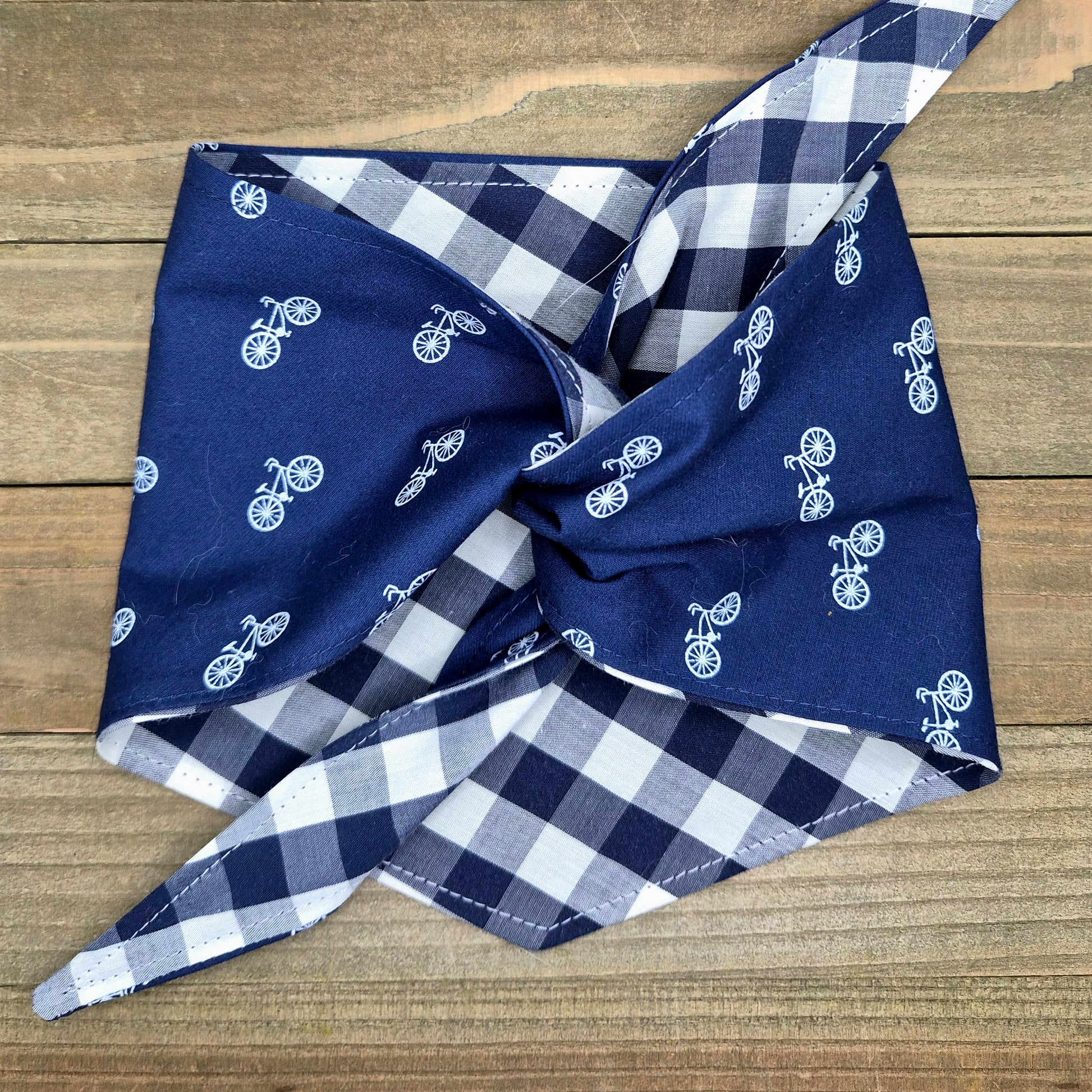 A blue and white checkered bandana with bicycle designs is folded and placed on a wooden surface.