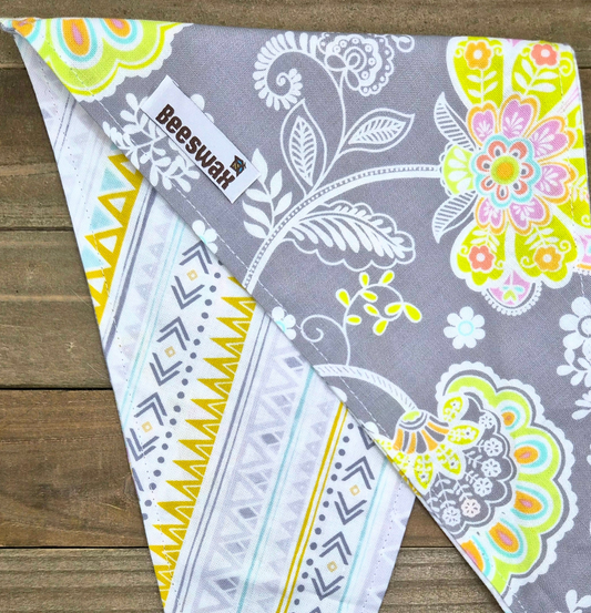 A colorful patterned bandana with a floral design and geometric shapes, resting on a wooden surface.