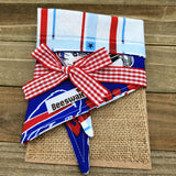 A red and white checkered bandana with a bow tied around it, placed on a burlap surface.