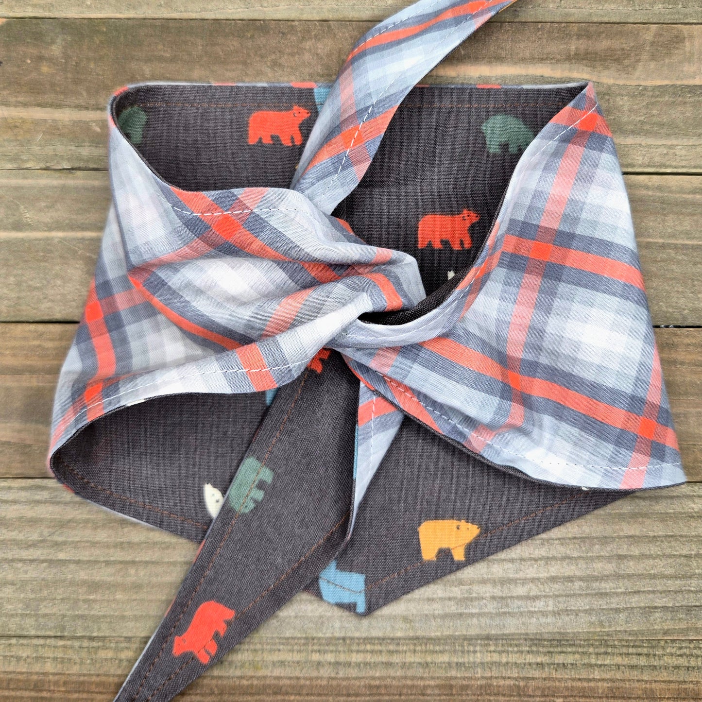 a plaid bandana with a pattern of bears in various colors, including orange, gray, and yellow, tied around a wooden surface.