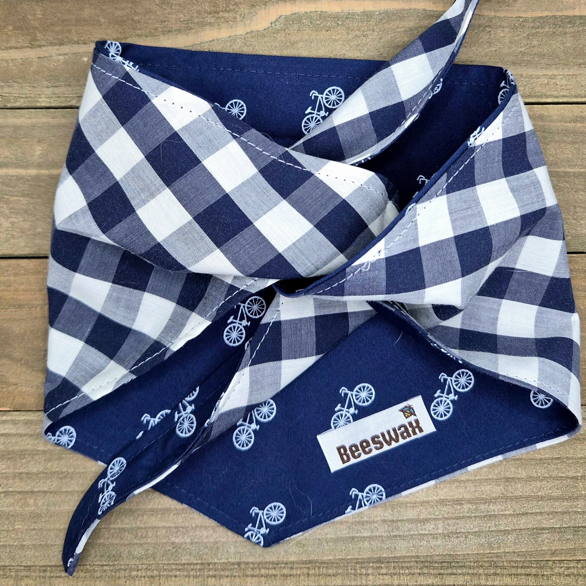 A blue and white checkered bandana with bicycle designs, folded and placed on a wooden surface.