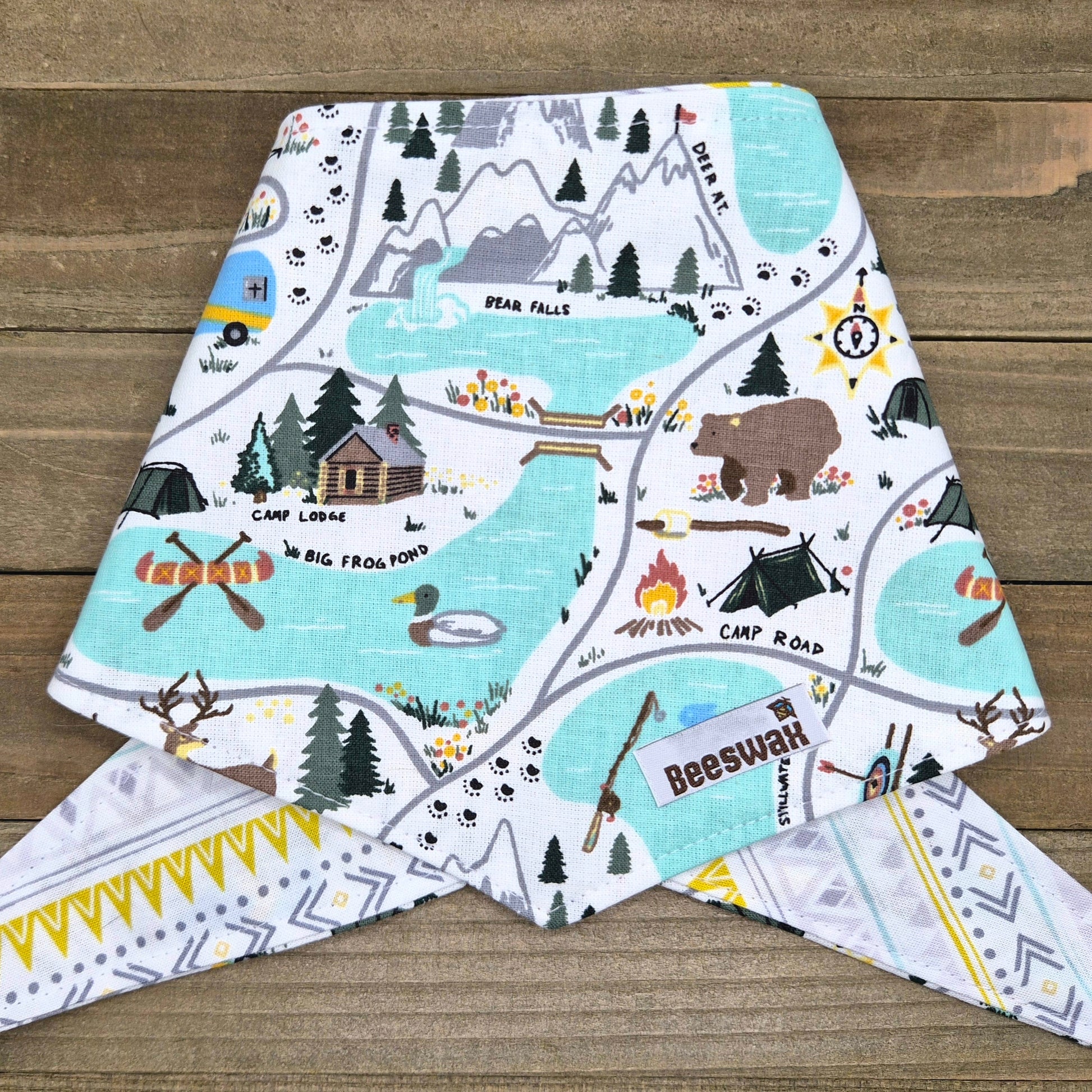 A colorful fabric bib featuring a map of a forest with various elements such as tents, campfires, and animals like bears and deer.