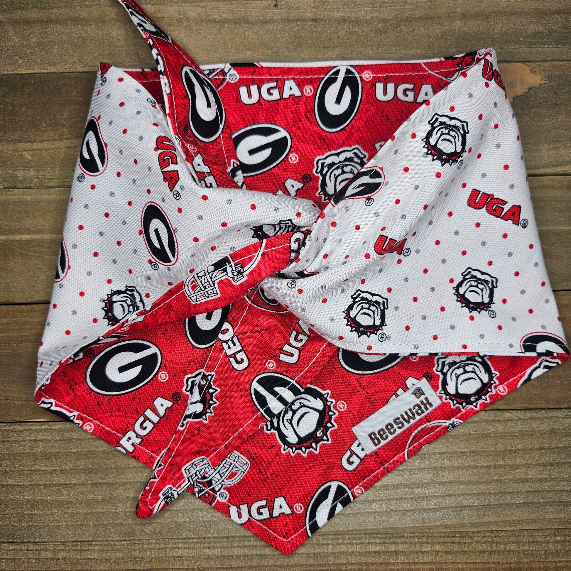 A red and white dog bandana with the Georgia Bulldogs logo printed on it, folded in half and tied around a wooden surface.
