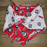 A red and white dog bandana with the Georgia Bulldogs logo printed on it, folded in half and tied around a wooden surface.