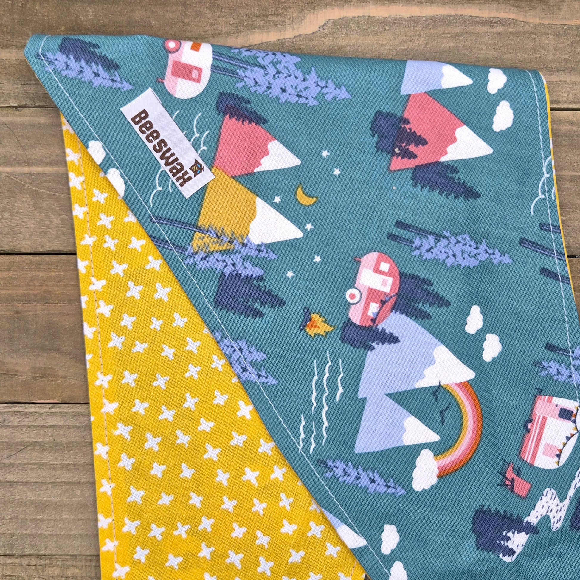 a colorful fabric with a pattern of mountains, clouds, and camping-related objects such as a camper van and tent.
