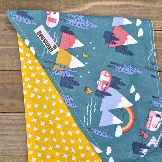 a colorful fabric with a pattern of mountains, clouds, and camping-related objects such as a camper van and tent.