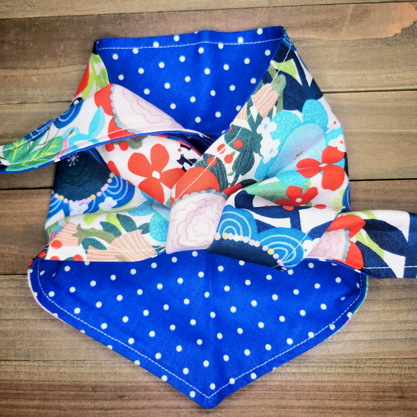 A colorful, patterned bandana with a blue and white polka dot fabric is displayed on a wooden surface.