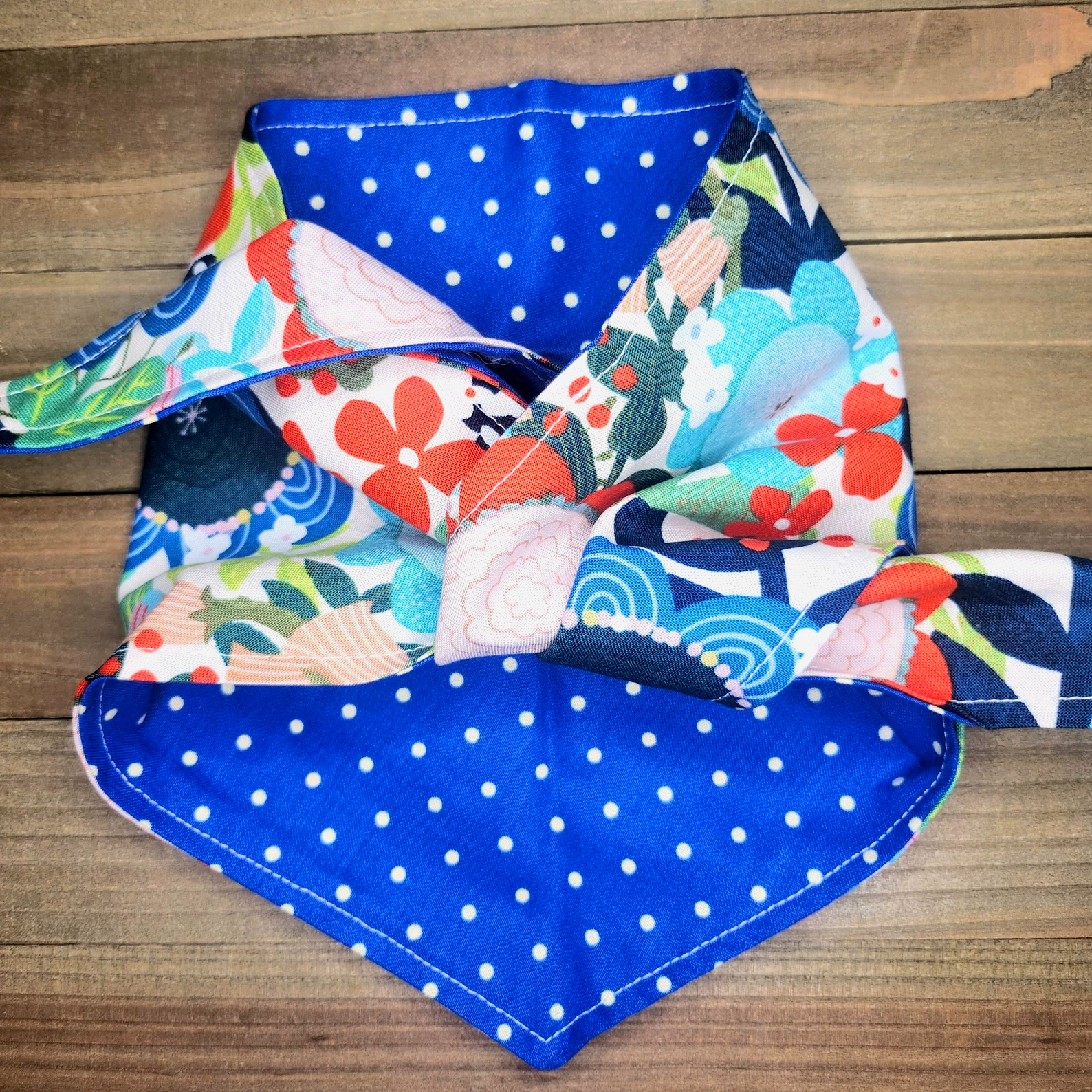 A colorful, patterned bandana with a blue and white polka dot fabric is displayed on a wooden surface.