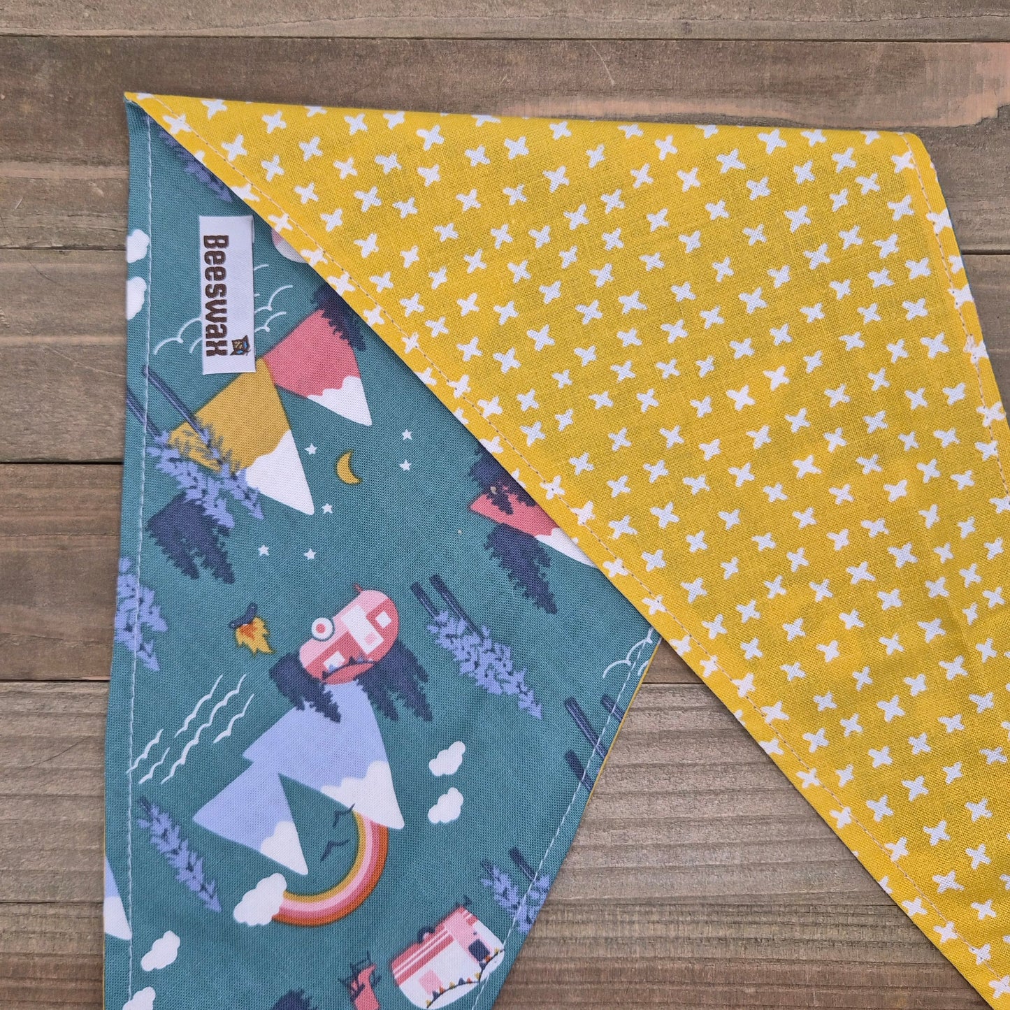 a colorful fabric with a pattern of mountains, trees, and a rainbow. The fabric is folded in half, with one side displaying a yellow pattern and the other side showing a blue pattern.