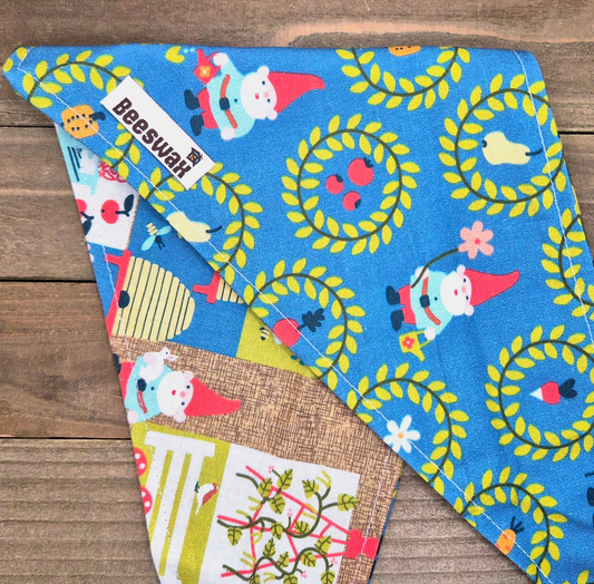 a blue fabric with a playful pattern of gnomes and flowers, including a gnome holding a basket of fruit.