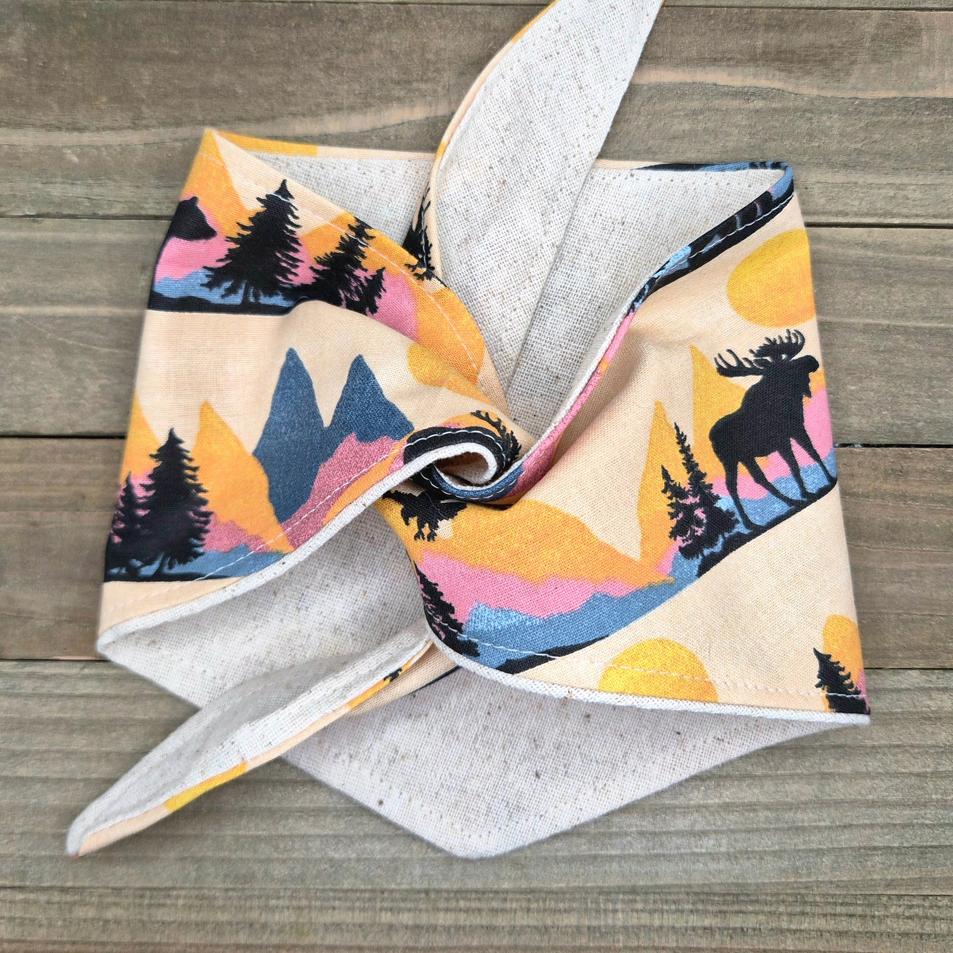 a colorful fabric with a pattern of trees and mountains, along with a moose silhouette. The fabric appears to be folded or twisted, creating a visually interesting design.